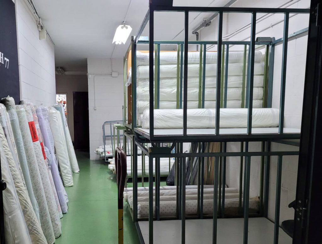 Interior del almacén de Texyahveh con rollos de tela almacenados de forma ordenada detrás de una estructura metálica, indicando una cuidadosa gestión del inventario.