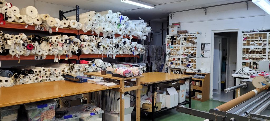 Área de trabajo y almacenaje de Texyahveh con estanterías de rollos de tela y equipo de corte, mostrando el compromiso con la calidad y eficiencia.